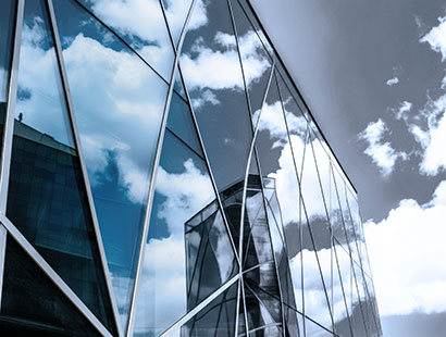 Blick von unten auf eine moderne Glasfassade mit geometrischem Muster. Der bewölkte Himmel spiegelt sich in den Glasflächen.